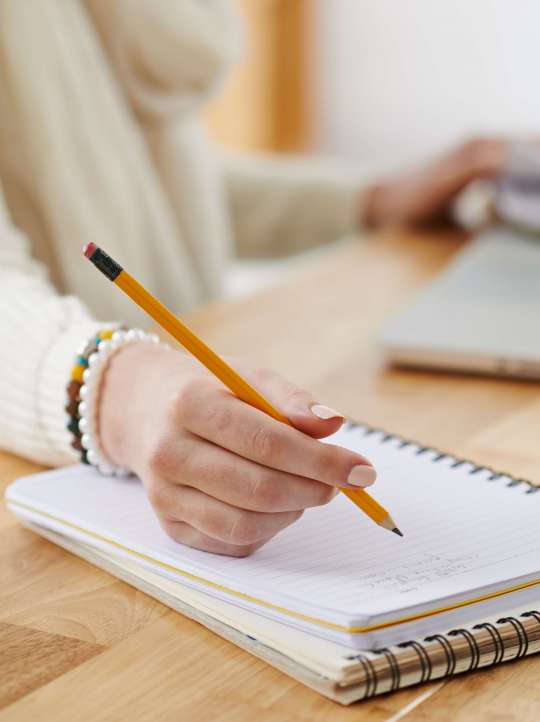Close-up image of female office worker writing plans in notepad, selective focus